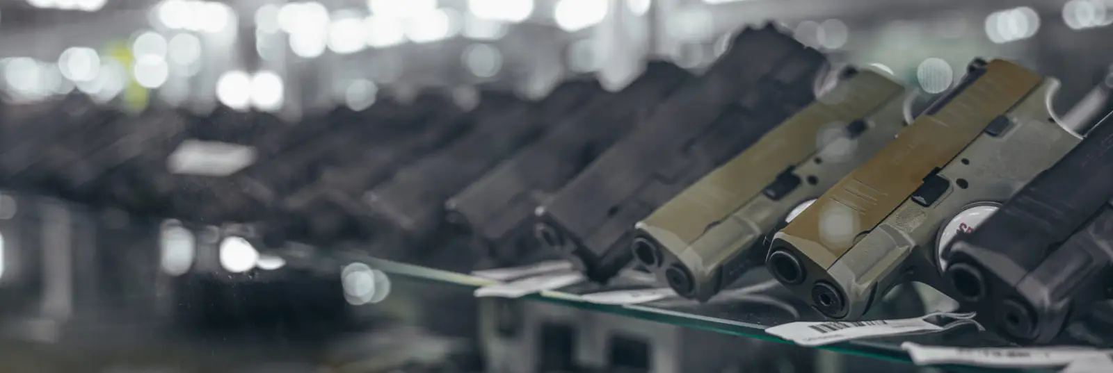 Firearms displayed in a glass case at a gun store, featuring rifles and handguns for rental and retail.